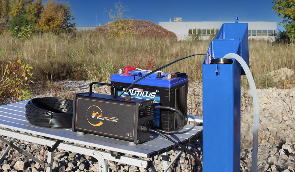 solinst 12v submersible pump on field table, connected to 12v marine battery beside blue monitoring well